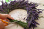 Feminine hands cutting the stems off of fresh lavender sprigs, fashioned into a wreath on a wooden table